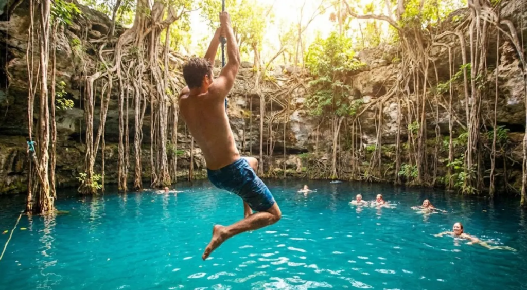 Hombre saltando con liana hacia las aguas turquesa del Cenote Oxman en Yucatán