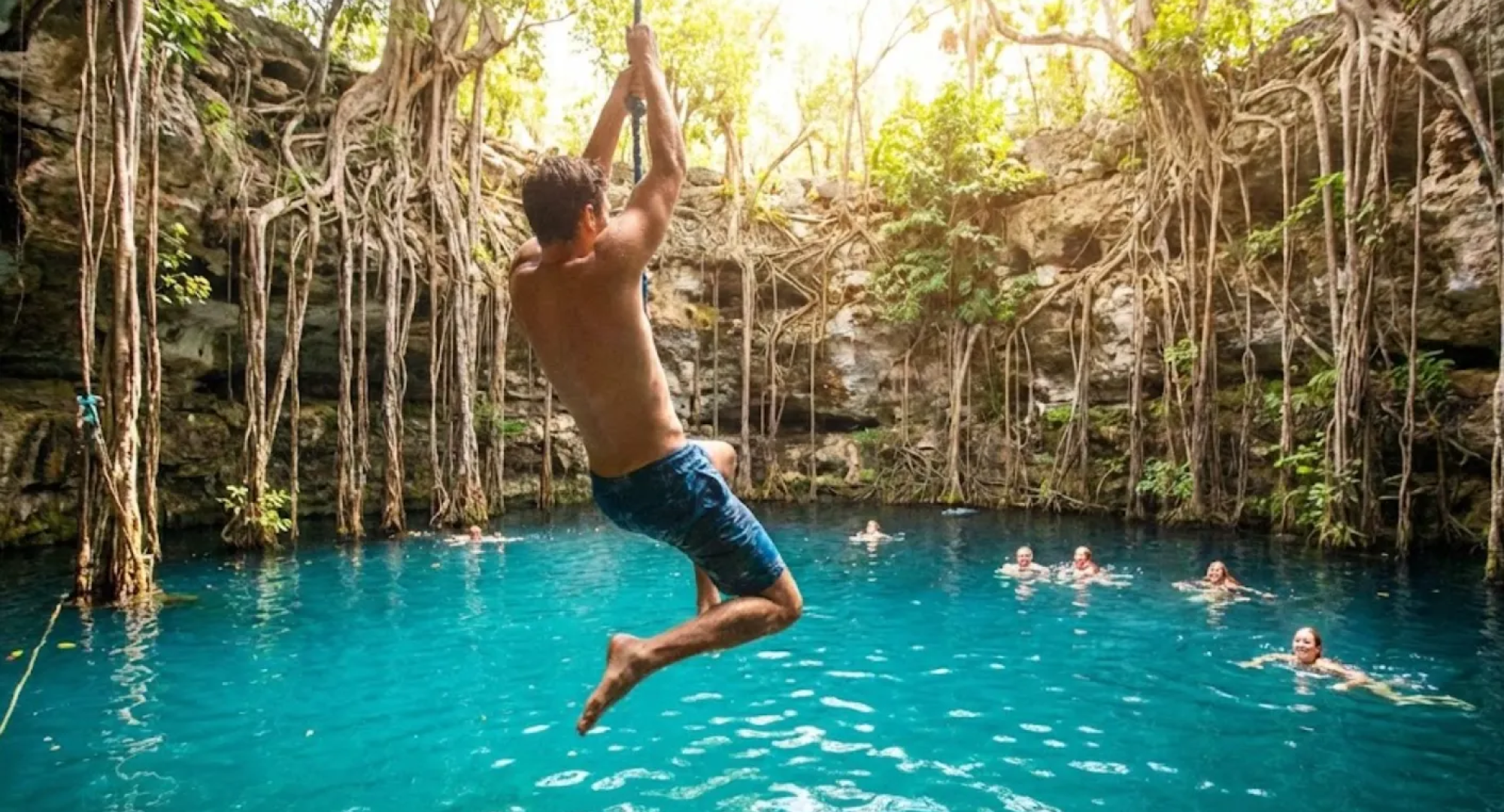 Hombre saltando con liana hacia las aguas turquesa del Cenote Oxman en Yucatán